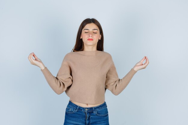 Signora meravigliosa che mostra gesto di meditazione in maglione, jeans e guardando rilassato, vista frontale.