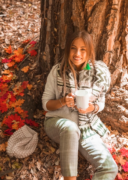 Signora sorridente con bevanda nella foresta di autunno