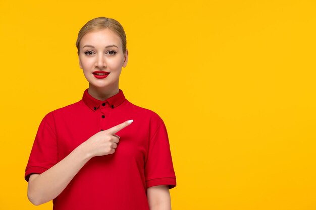 Signora sorridente di giorno della camicia rossa che mostra a destra in una camicia rossa su una priorità bassa gialla