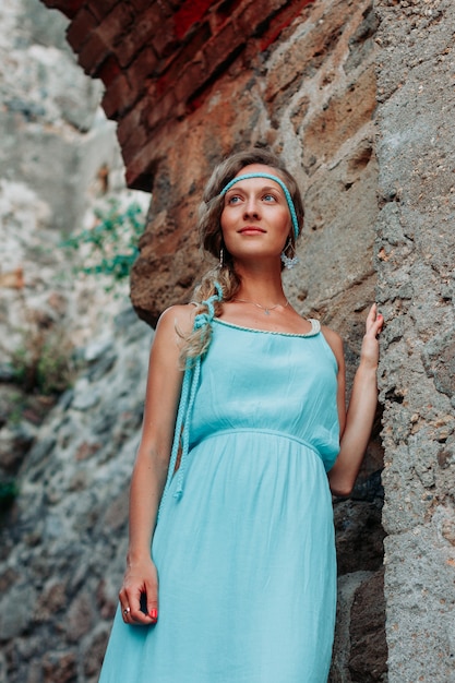 Signora splendida che si appoggia sulla parete e che sorride in vestito blu lungo durante il giorno.