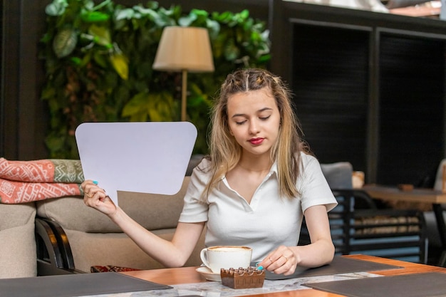 Signora sveglia che si siede al ristorante e che tiene il bordo bianco dell'idea