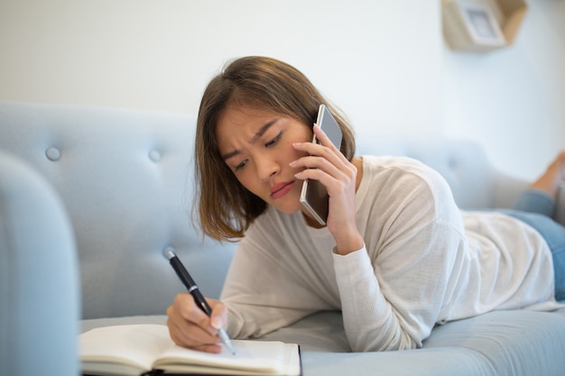 Signora tesa che fa le note e che chiama sul telefono sul sofà