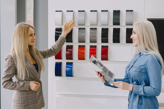 Signore in un salone di automobile. Donna che compra l'auto. Donna elegante in un vestito blu. Il manager aiuta il cliente.