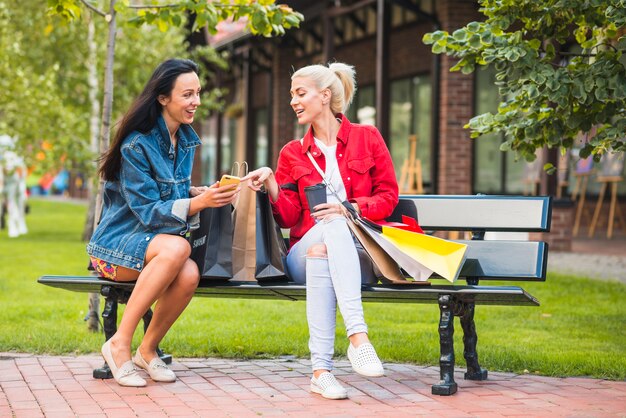 Signore sorridenti guardando smartphone sulla panchina