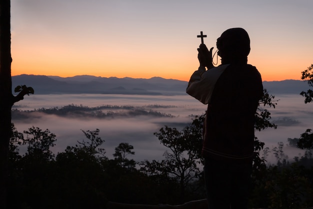 Silhouette della mano umana che tiene la croce, lo sfondo è l'alba