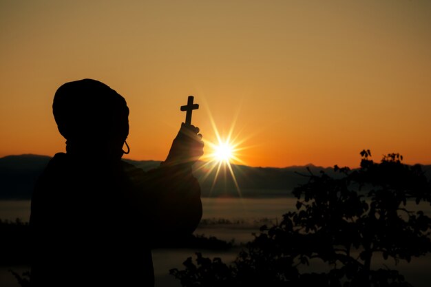 Silhouette della mano umana che tiene la croce, lo sfondo è l'alba