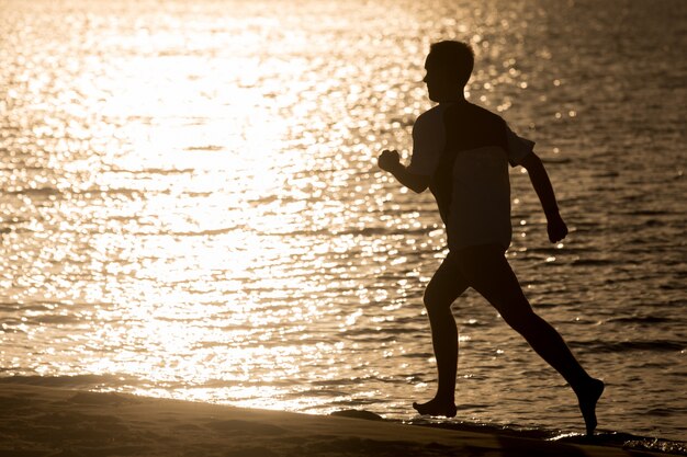 Silhouette di giovane uomo che fa jogging in riva al mare