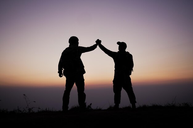 Silhouette di lavoro di squadra aiutando la mano fiducia aiuta Successo in montagna Gli escursionisti festeggiano con le mani in alto Aiutarsi a vicenda in cima al paesaggio di montagna e tramonto