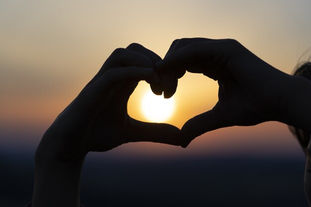 Silhouette di mani che formano un cuore al tramonto