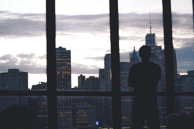 Silhouette di un successo maschile in piedi di una finestra che domina l'isola di Manhattan