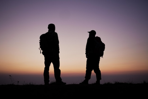 Silhouette di uomini escursionista con zaino rimanere sulla scogliera e pensare sulla montagna in cima al tramonto stile di vita di viaggio voglia di viaggiare concetto di avventura vacanze estive all'aperto