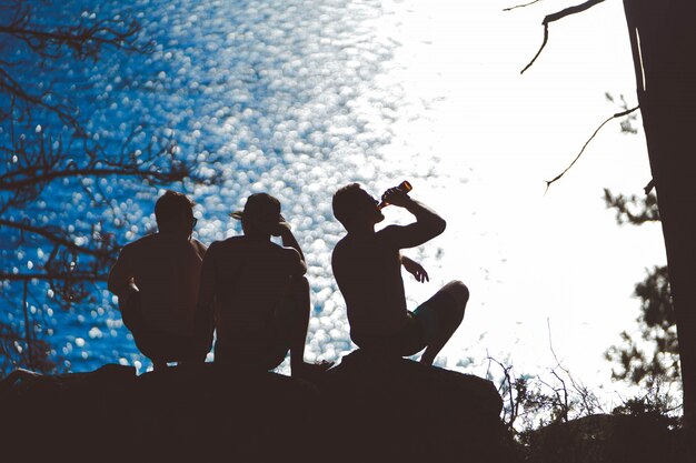 Silhouette orizzontale di tre amici che vanno in giro vicino al mare e bevono birra la sera