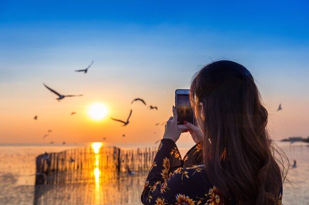 Silhoutte di uccelli che volano e giovane donna che cattura una foto al tramonto.