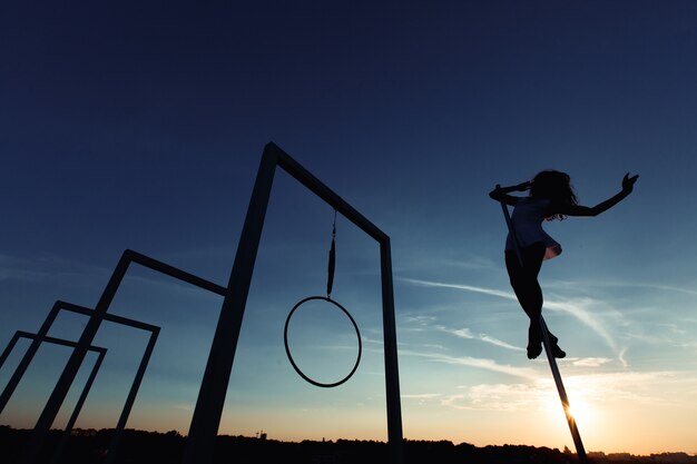 Siluetta del ballerino del palo sexy che esegue sul tetto al tramonto