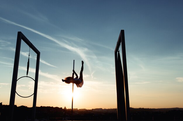 Siluetta del ballerino del palo sexy che esegue sul tetto al tramonto