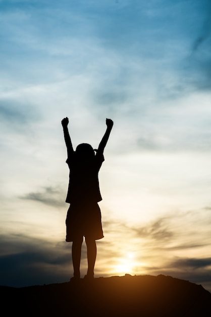 Siluetta della bambina che solleva mano al tempo felice di libertà