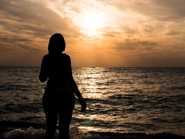 Siluetta della donna che guarda il sole sulla spiaggia al tramonto... Ragazza turistica in vacanza al mare