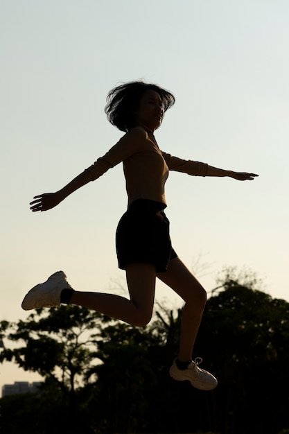 Siluetta della donna del colpo pieno che salta al tramonto