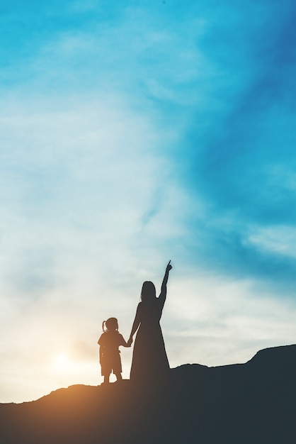 Siluetta della madre con sua figlia in piedi e tramonto