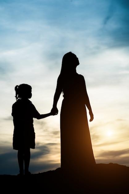 Siluetta della madre con sua figlia in piedi e tramonto