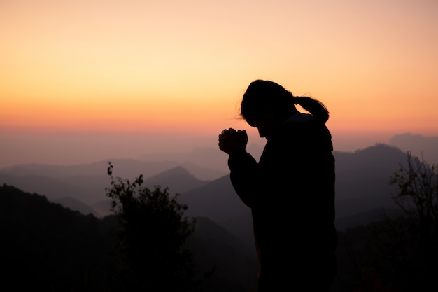 Siluetta della ragazza che prega sopra la bella priorità bassa del cielo.