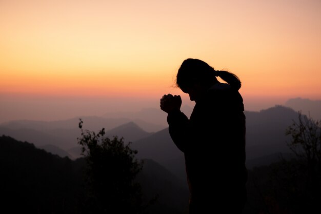 Siluetta della ragazza che prega sopra la bella priorità bassa del cielo.