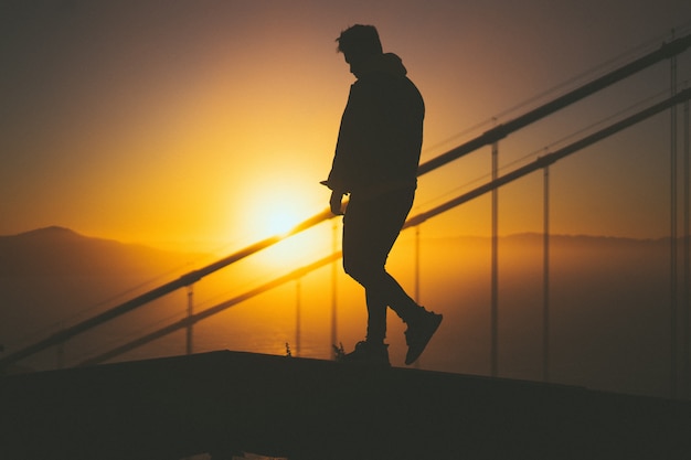 Siluetta di giovane maschio che cammina sulla scala dietro le rotaie della scala con la bella vista di tramonto