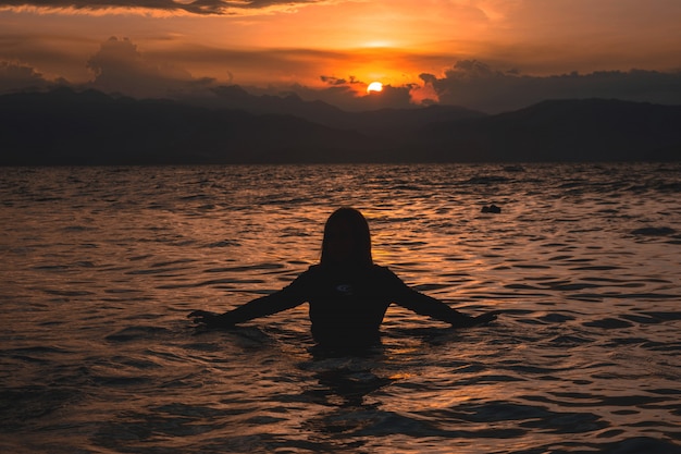 Siluetta di una metà femminile nell'acqua di un mare durante un bel tramonto