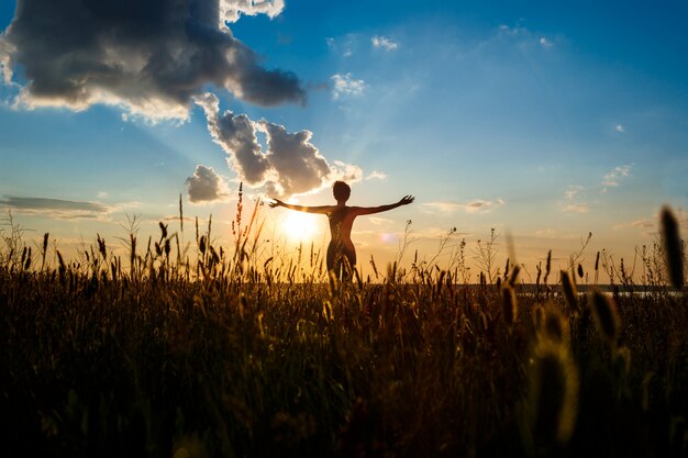 Siluetta di yoga di pratica della ragazza allegra nel campo ad alba.