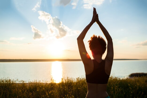 Siluetta di yoga di pratica della ragazza allegra nel campo ad alba.