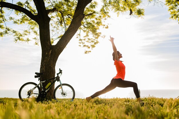 Siluetta sottile della bella donna che fa sport nella mattina nel parco che fa yoga