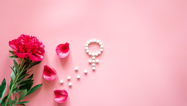 Simbolo di Venere di genere fatto di pillole e fiore di peonia su sfondo rosa