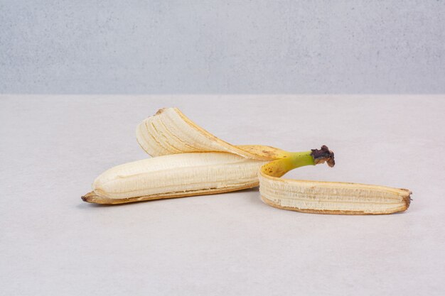 Singola banana sbucciata sulla tavola bianca.