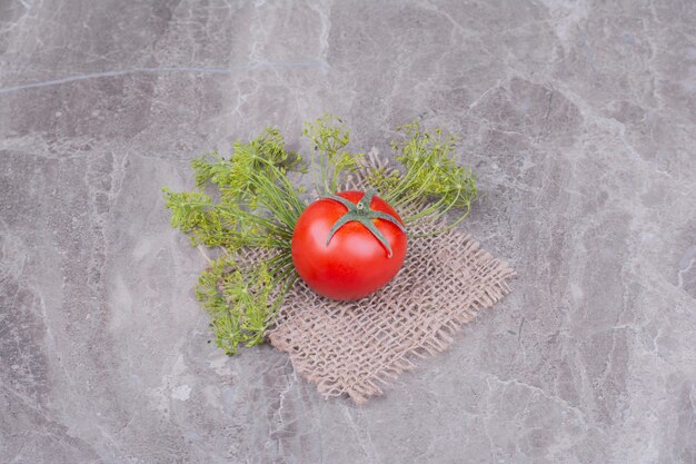 Singolo pomodoro rosso con erbe su un pezzo di tela.