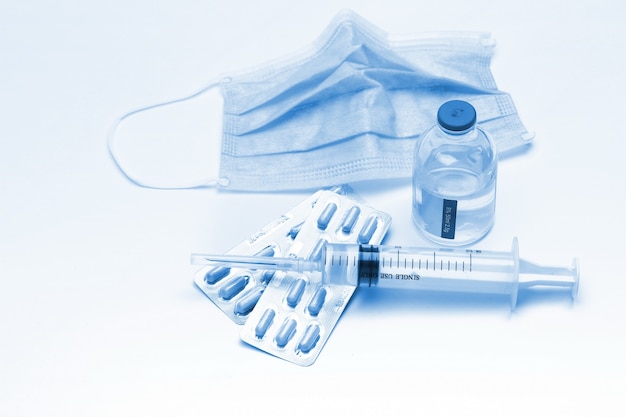 Siringa, capsule e bottiglia di maschera medica su sfondo bianco