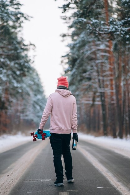 Skateboarder in piedi sulla strada in mezzo alla foresta circondata dalla neve