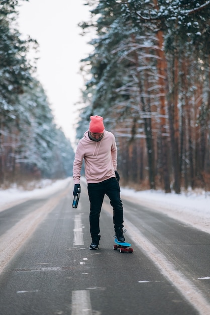 Skateboarder in piedi sulla strada in mezzo alla foresta circondata dalla neve