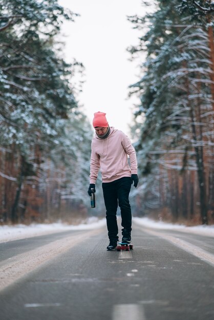 Skateboarder in piedi sulla strada in mezzo alla foresta circondata dalla neve