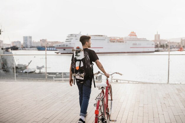 Skateboarder maschio che cammina con la bicicletta vicino alla costa