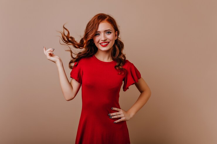 Foto gratuito slim donna caucasica in abito rosso ridendo. splendida ragazza dello zenzero che gioca con i suoi capelli durante il servizio fotografico.