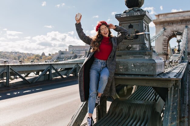 Slim donna che ride in jeans vintage in posa su sfondo di architettura in una giornata di sole a Parigi