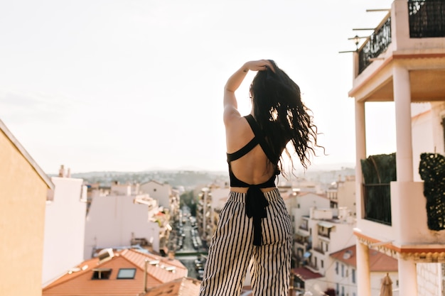 Slim ragazza elegante con lunghi capelli scuri godendo della vista sulla città dal ponte di osservazione al mattino