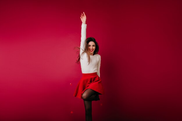 Slim ragazza felice in maglione bianco che salta sullo spazio bordeaux