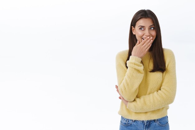 Sly cute brunette caucasica ridacchia e copre la bocca con un sorriso orribile mentre sbircia a sinistra ridendo di qualcuno che spettegola sul goffo collega in piedi gioioso su sfondo bianco