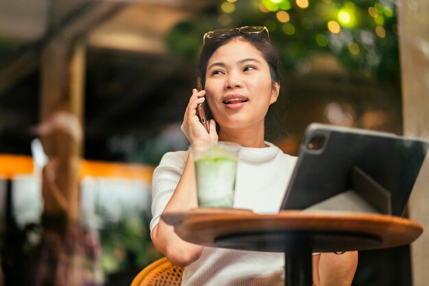 Smart attraente positivo asiatico nomade digitale femmina che indossa un panno casual lavoro remoto nuovo stile di vita normale uso manuale tablet teleconferenza onlive videochiamata riunione remota al coffeeshop cafe