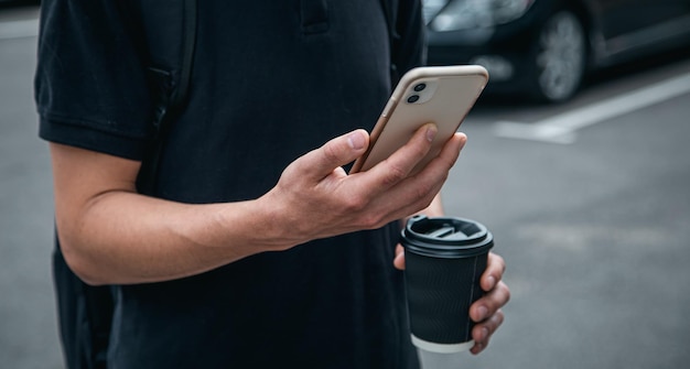 Smartphone del primo piano e un bicchiere di caffè nelle mani di un uomo