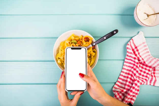 Smartphone della holding della mano della donna sopra la pasta di tagliatelle