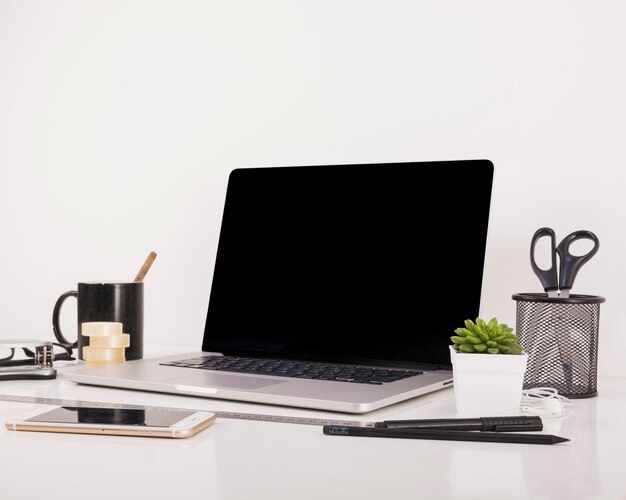 Smartphone e computer portatile con lo schermo nero in bianco sulla scrivania