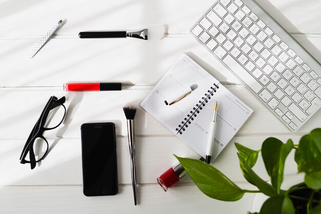 Smartphone e occhiali vicino a cosmetici e tastiera