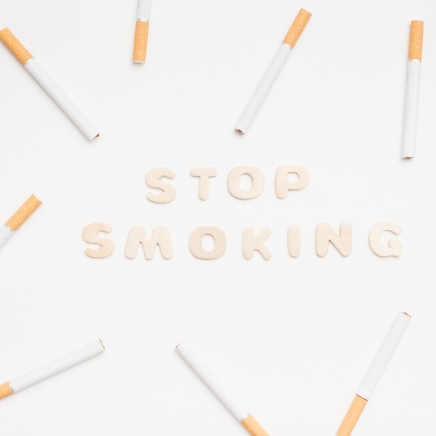Smetta di fumare il testo circondato dalle sigarette contro fondo bianco